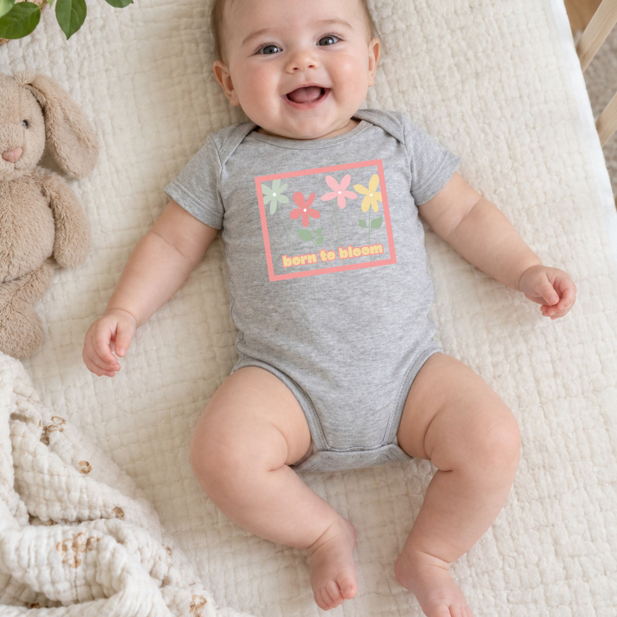Baby wearing a heather gray Born to Bloom infant bodysuit with a colorful retro flower design.