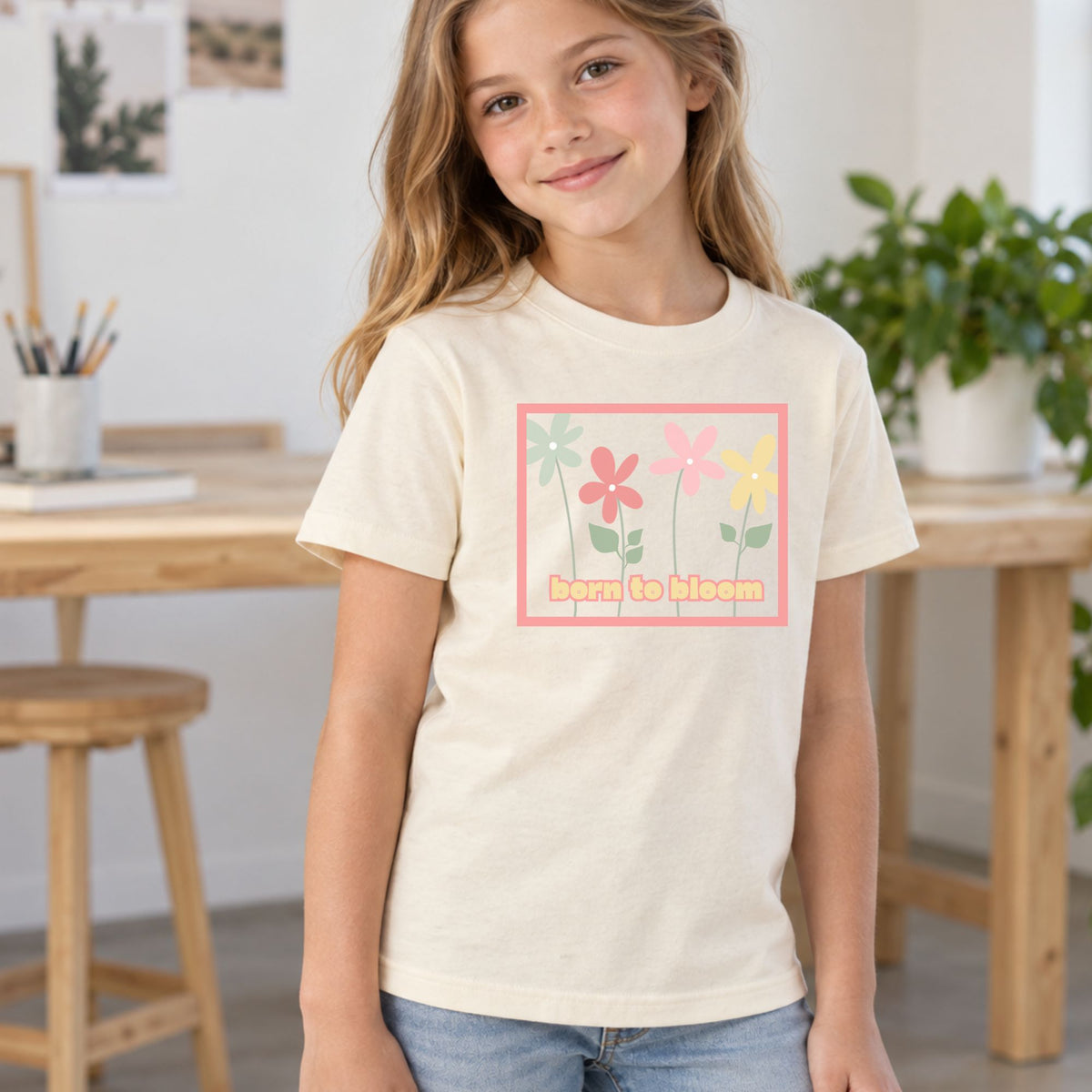 Youth model wearing a natural Born to Bloom short sleeve tee, front view showing the colorful retro flower design.
