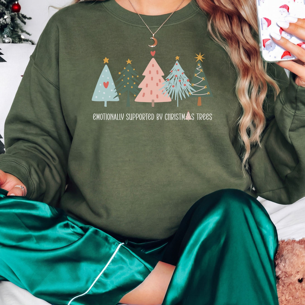 Woman wearing a forest green Emotionally Supported by Christmas Trees adult crewneck sweatshirt with green holiday pajamas.
