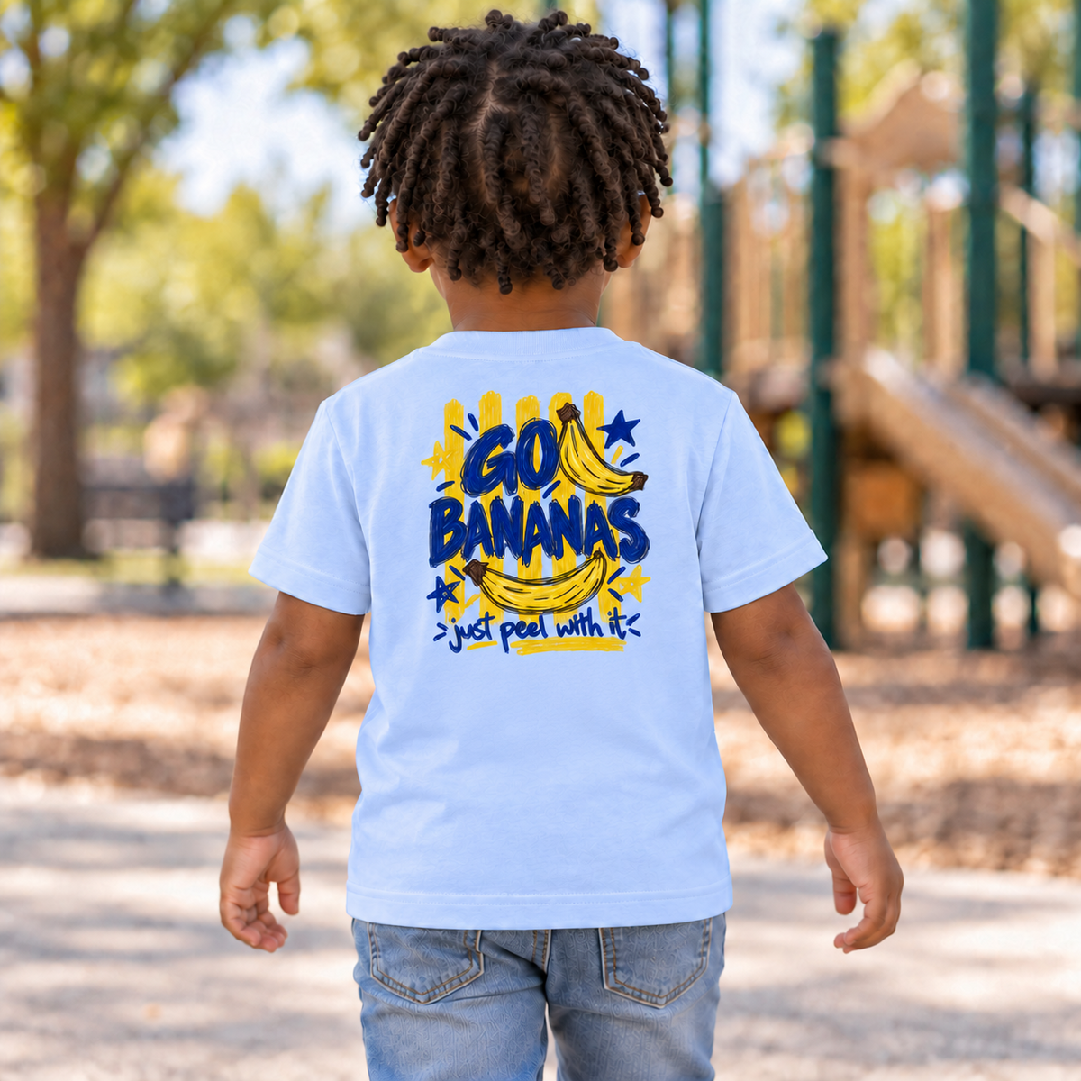 Toddler wearing a light blue Go Bananas short sleeve tee, back view showing the full banana design with “Just Peel With It.”