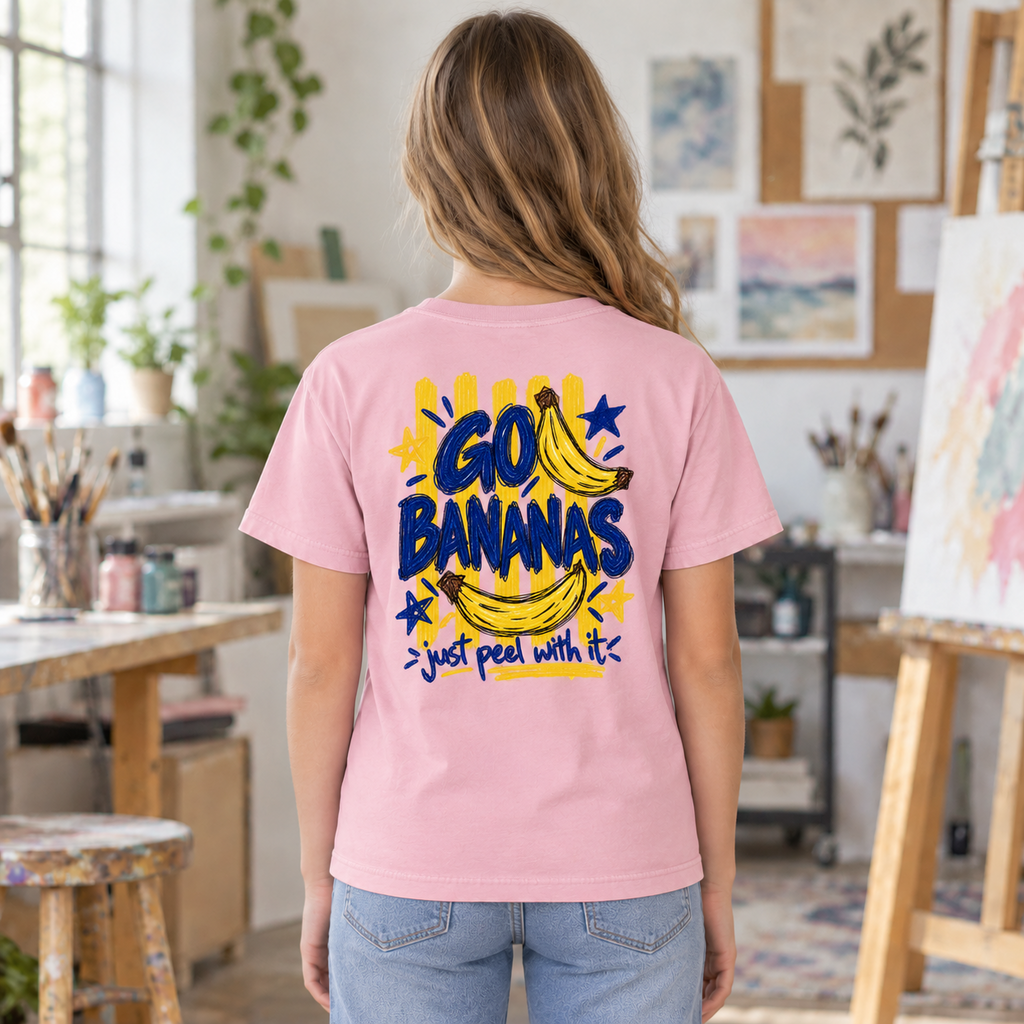 Youth wearing a soft pink Go Bananas tee, back view showing the full banana design with “Just Peel With It.”