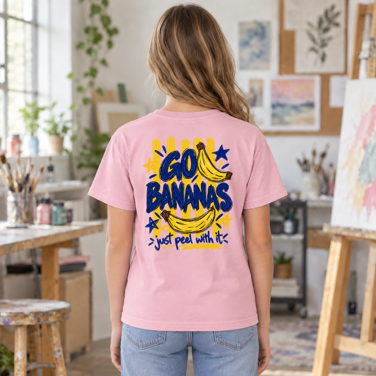 Youth wearing a soft pink Go Bananas tee, back view showing the full banana design with “Just Peel With It.”