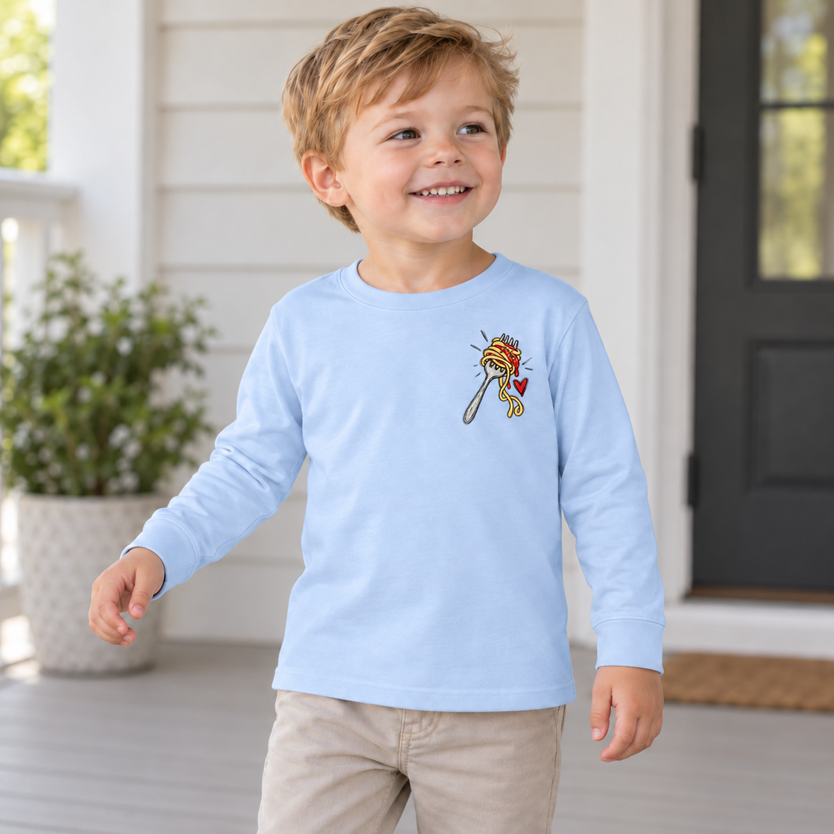 Toddler wearing a light blue No Regretti long sleeve tee, front view showing the spaghetti left-chest design.