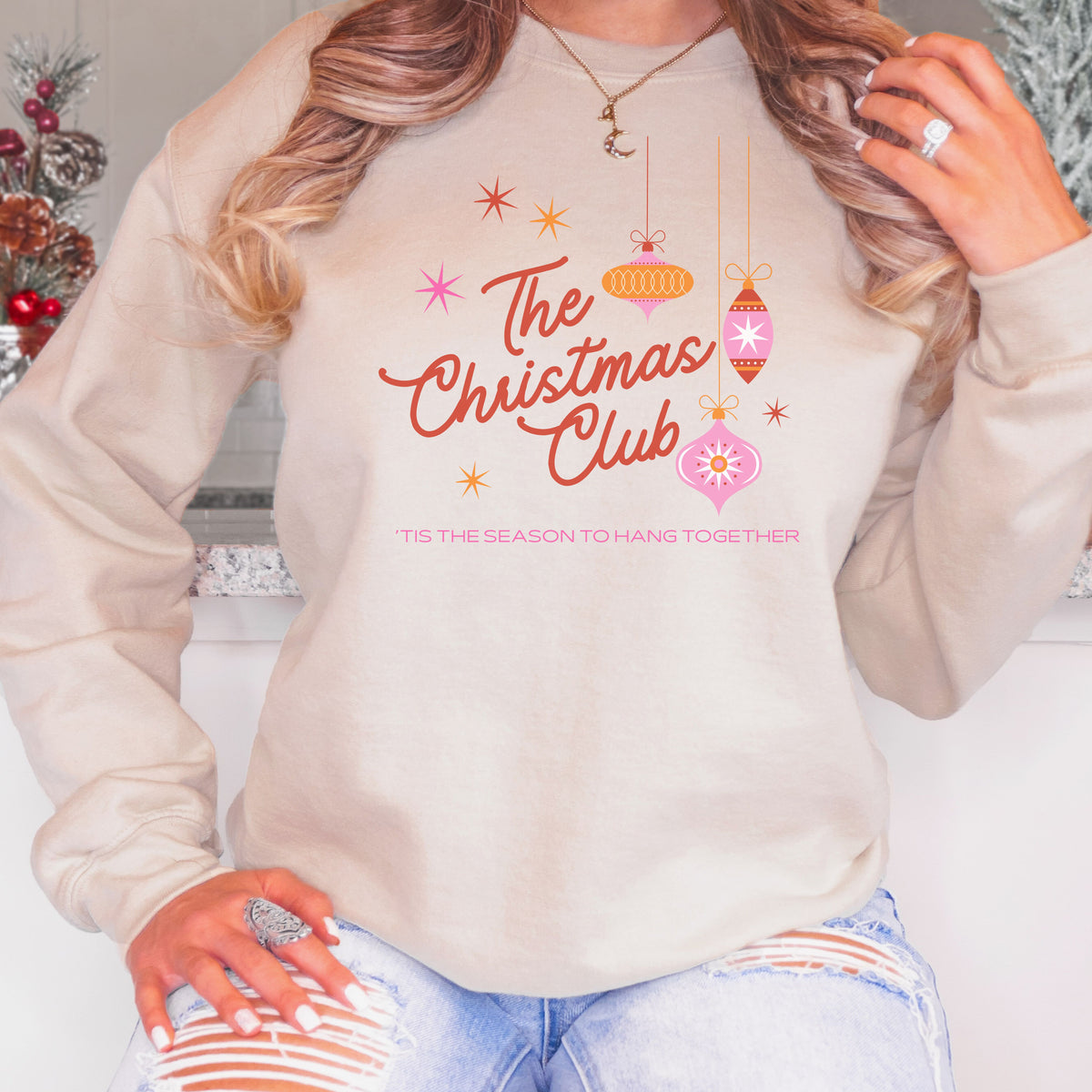 Woman wearing a sand The Christmas Club ’Tis the Season to Hang Together adult crewneck sweatshirt.